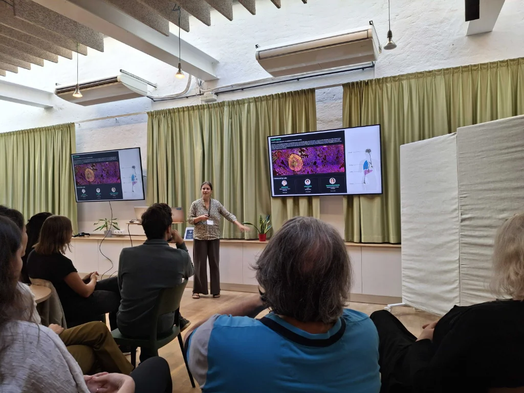 Juliane Winkler presenting the MetPredict project in front of screens showing a multiplexed image of breast cancer tissue.