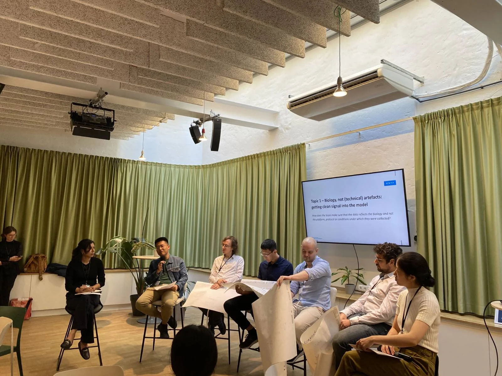 Panel of researchers seated in front of a screen showing "Topic 1 - Biology, not (technical) artefacts: getting clean signal into the model".
